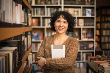 Portrait of smiling in library holding a book. Looking at camera. - 409859804