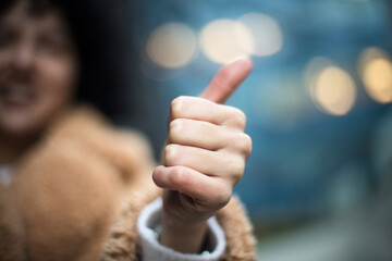 Woman showing Thumbs Up on street. Focus is on hand.