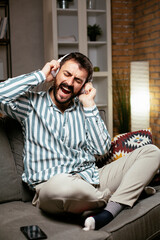 Obraz premium Young man with headphones resting on sofa. Happy man singing and listening the music.