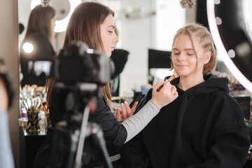 Woman making a video for her blog of making makeup, digital camera on tripod. Young female blogger on camera screen while doing makeup