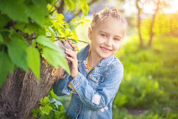 Beatiful smiling child girl hiding behind a tree in local park