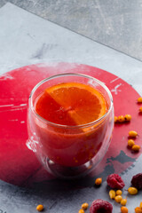 Grapefruit herbal tea with spices and honey in glass cup on a grey background, red hot drink with orange, a Japanese traditional drink