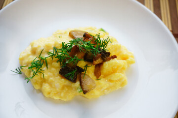 Close-up of appetizing scrambled eggs with mushrooms and dill on a white plate. Healthy protein breakfast. Home cooking concept.