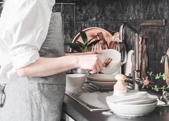 Woman washes dishes with wooden brush