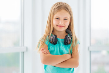 Dreaming little girl with headphones on her neck and arms crossed