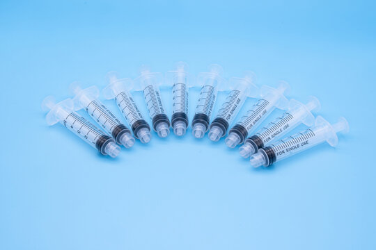 multiple clear plastic 5ml syringes isolated against a blue background