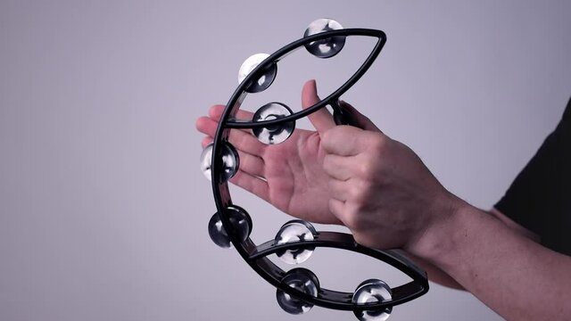 Caucasian hands holding and playing a black half moon shaped tambourine
