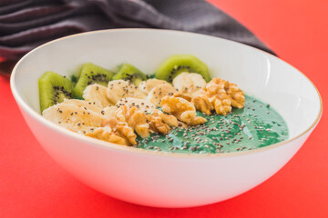 spirulina smoothie bowl with banana, walnuts, kiwi and chia seeds on red background