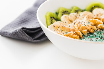 spirulina smoothie bowl with banana, walnuts, kiwi and chia seeds on white background