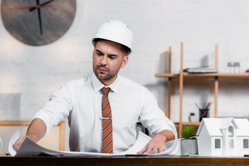 concentrated architect in helmet working on project near house model