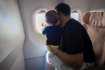 father and cute Toddler sitting on an airplane and looking at the sky through the porthole. first flight concept, traveling with children