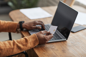 Close up of unrecognizable African-American man holding mockup credit card while online shopping...
