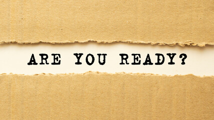 Text ARE YOU READY appearing behind torn brown paper. Top view.