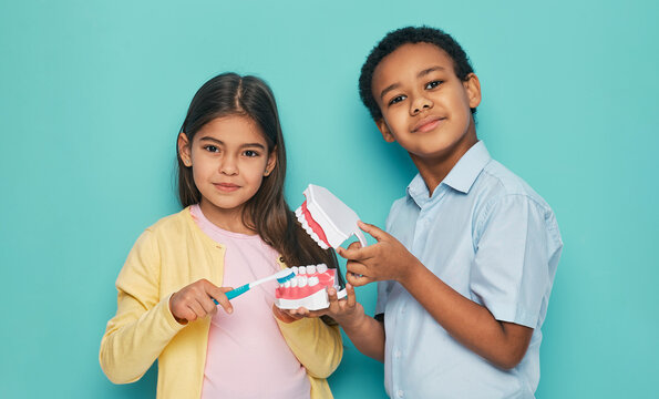 Two multiethnic kids show how to brush teeth properly and oral hygiene, isolated on turquoise background