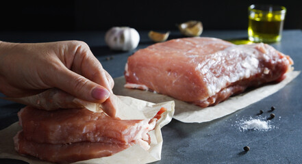 Cooking food. A woman's hand wraps chopped steaks in paper. Fresh raw meat with spices against a dark background.
