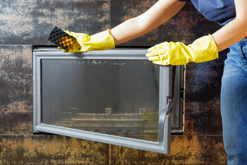 Homework. A woman in blue jeans, yellow gloves on her hands, cleans the heat-resistant glass of the...
