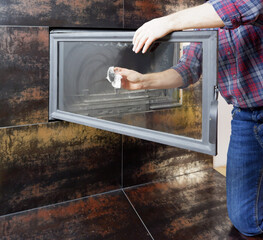 A man in a shirt and blue jeans cleans the heat-resistant glass of a modern fireplace. Close-up...