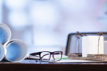 selective focus of eyeglasses near rolled blueprints on desk in office