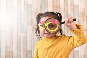 Cute little asian girl looking through a magnifying glass. Concept of curiosity child learning and eyesight