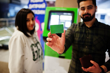 Indian couple performs transactions from the bank atm. Man show green credit card.