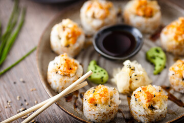 Baked sushi maki rolls with prawns and crab on a plate with chopsticks, soy sauce, wasabi and ginger. Japanese traditional fish food closeup served for lunch in modern gourmet restaurant