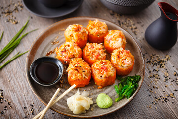 Baked sushi maki rolls with salmon, crab, cucumber, avocado, flying fish roe and spicy sauce on a plate with chopsticks, soy sauce, wasabi and ginger. Japanese seafood served for lunch in restaurant