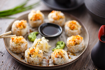 Baked sushi maki rolls with prawns and crab on a plate with chopsticks, soy sauce, wasabi and ginger. Japanese traditional fish food closeup served for lunch in modern gourmet restaurant