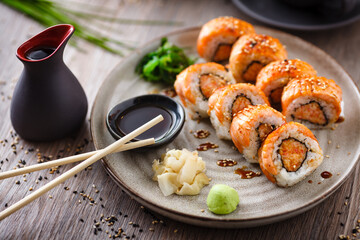 Baked sushi maki rolls with salmon, crab and spicy sauce on a plate with chopsticks, soy sauce, wasabi and ginger. Japanese traditional fish food closeup served for lunch in modern gourmet restaurant