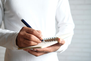 Close up of man in casual white shirt writing on notepad.