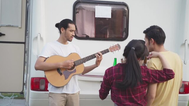 Group of friends playing guitar and singing a song at outdoor party.