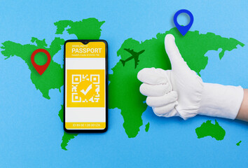 Electronic Immunity passport with a COVID-19 vaccination stamp on a smartphone screen with passport on the world map and hand in gloves shows thumb up. Flat lay. Concept of vaccination of coronavirus