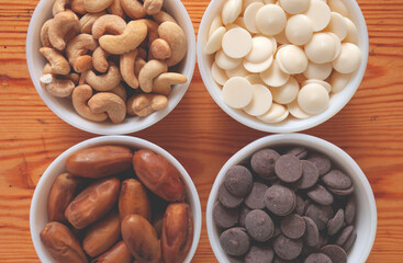 Food ingredients in white bowls. Cashews, dates, white and milk chocolate drops in white small bowls.