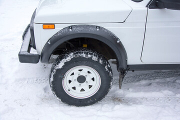 Front winter snow-covered wheel of white SUV on white beautiful drive with the front of the car