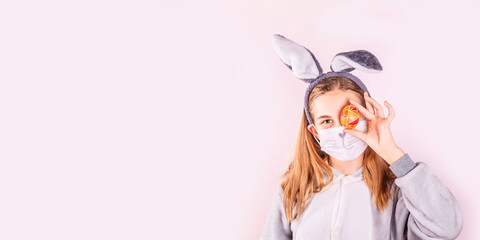 Girl in rabbit bunny ears on head and protective mask with colored eggs on pink background. Covid Easter holiday banner