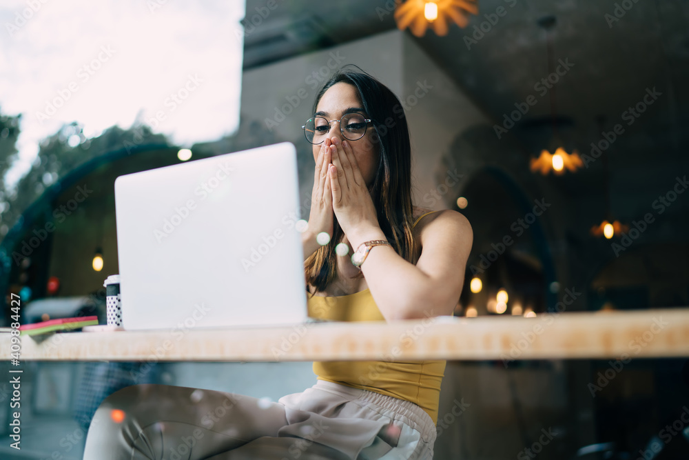 Poster amazed hipster girl in spectacles shocked with received email news on modern netbook for networking 
