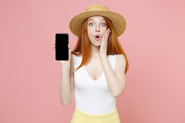 Young shocked surprised redhead woman 20s in straw hat summer clothes touch face holding hand texting mobile cell phone blank screen workspace area isolated on pastel pink background studio portrait