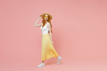 Full length body young redhead ginger woman in straw hat glasses summer clothes yellow pleated maxi skirt looking camera walking going passing isolated on pastel pink color background studio portrait. - Powered by Adobe