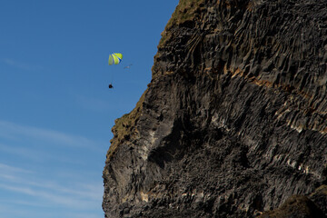 Sky-diver seen floating down after jumping from the high Reynisdrangar sea cliff during a sunny...