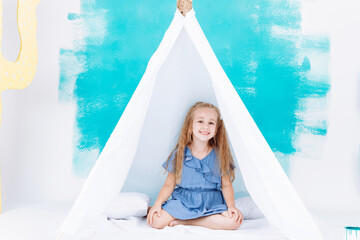 Portrait of a beautiful smiling little girl. Little girl playing in a white wigwam on colorful wall background. Fun lovely child having fun in children room. happy childhood © Andriy Medvediuk