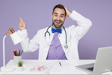 Male doctor man in white medical suit sits at desk work on computer in clinic office point index...