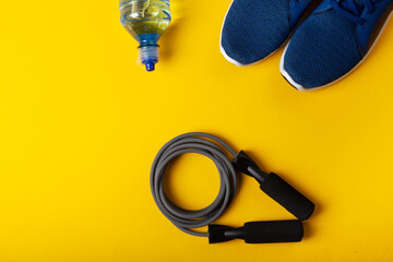 Blue sneakers, skipping rope and bottle of water on yellow background. Concept of healthy...