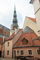 Obraz premium Famous view on latvian highest unique medieval and gothic architecture church tower with clock and the roofs of old houses on street in the center of capital old city Riga, Latvia, the Baltic region
