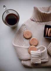 women's beige turtleneck lies on a white background with a cup of coffee and cookies