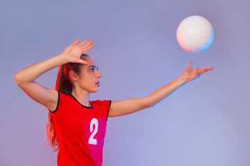 Volleyball girl hold and kick ball on neon background. Player doing sport workout at home. Sport and recreation concept