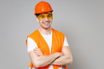 Young employee smiling man in orange vest protective hardhat look camera hold hands crossed folded isolated on grey background studio portrait Instruments for renovation apartment Repair home concept.