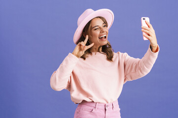 Happy girl showing peace sign while taking selfie on cellphone