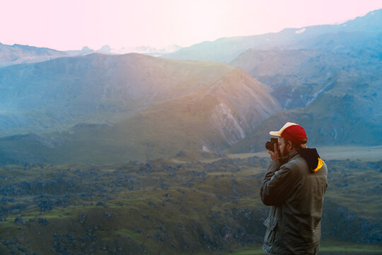 A man in a jacket and a cap takes pictures of the mountains