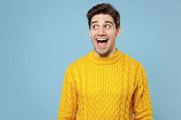 Young surprised funny attractive cheerful friendly student man 20s wearing casual knitted cozy yellow fashionable sweater looking aside with smile isolated on blue color background studio portrait