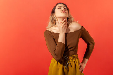 POrtrait of sad woman with blonde hair and closed eyes palping neck feeling throat ache and pain during swallow, tonsillitis inflammation. Indoor studio shot isolated on red background