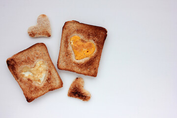 Toast bread with frighten egg in a heart shaped hole on round wooden board on white background. Creative Valentine's day or Mothers day breakfast idea